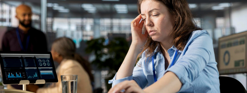 funcionária em mesa de escritório com aspecto de cansaço físico e mental
