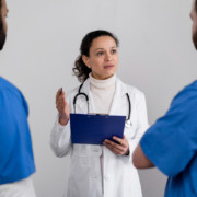 médica ao centro, de branco, conversando com dois médicos em sua frente