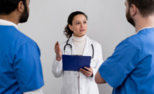 médica ao centro, de branco, conversando com dois médicos em sua frente