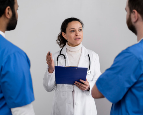 médica ao centro, de branco, conversando com dois médicos em sua frente