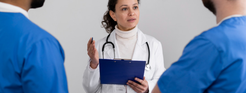 médica ao centro, de branco, conversando com dois médicos em sua frente