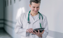 médico jovem de jaleco em corredor de hospital utilizando tablet