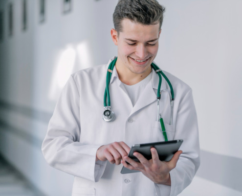 médico jovem de jaleco em corredor de hospital utilizando tablet