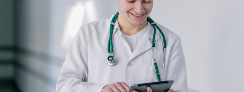 médico jovem de jaleco em corredor de hospital utilizando tablet