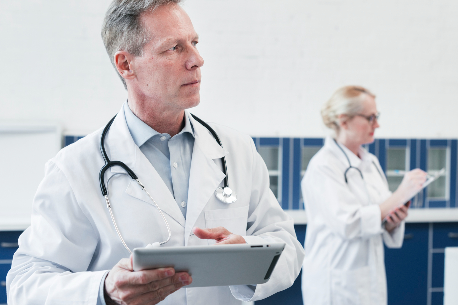 médico segurando prancheta com médica ao fundo conferindo anotações