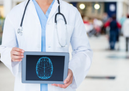 médico em pé, de jaleco branco com tela de tablet em mãos