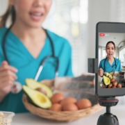 médica na cozinha, com legumes e gravando vídeo no celular