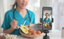 médica na cozinha, com legumes e gravando vídeo no celular