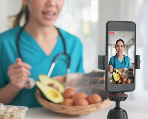 médica na cozinha, com legumes e gravando vídeo no celular