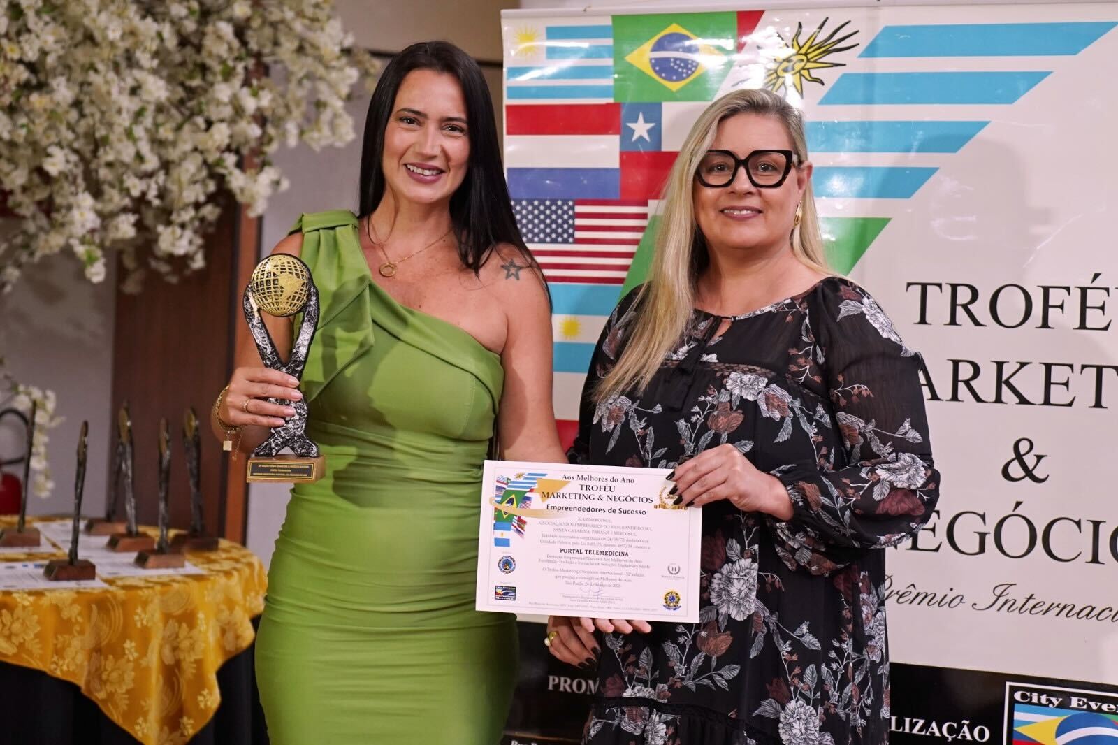 duas mulheres em premiação segurando um certificado no palco