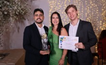 três pessoas em pé com roupa esporte fino, recebendo prêmio com troféu em mãos