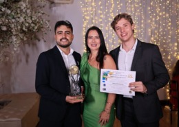 três pessoas em pé com roupa esporte fino, recebendo prêmio com troféu em mãos