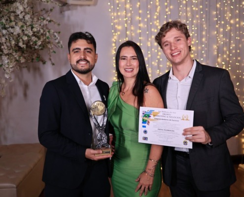 três pessoas em pé com roupa esporte fino, recebendo prêmio com troféu em mãos