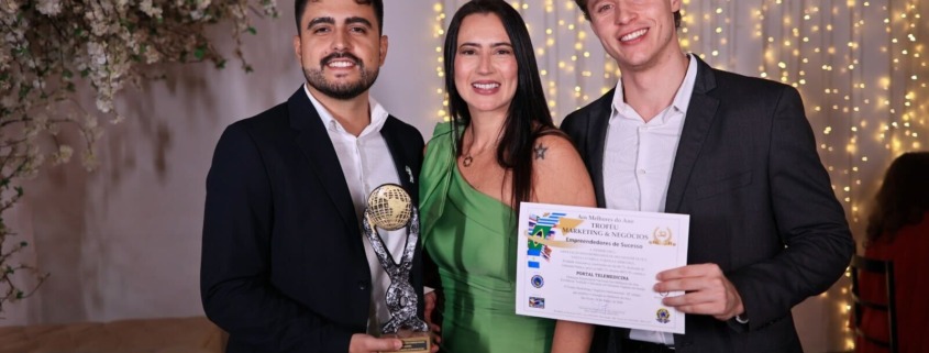 três pessoas em pé com roupa esporte fino, recebendo prêmio com troféu em mãos