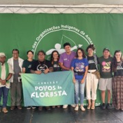 grupo de pessoas reunidas para foto em palco com uma bandeira verde ao fundo