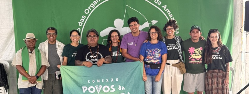 grupo de pessoas reunidas para foto em palco com uma bandeira verde ao fundo