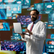médico em pé na sala rodeado de telas com dados e gráficos digitais, simbolizando a tecnologia