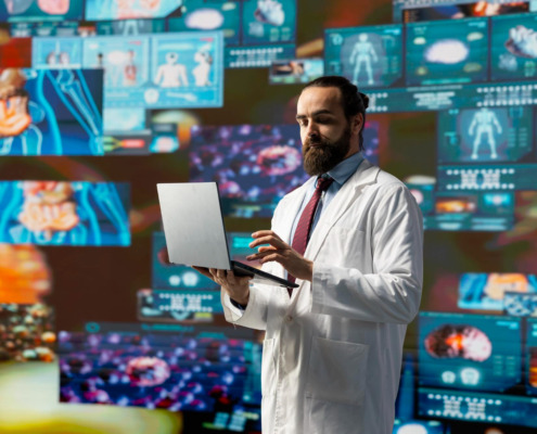 médico em pé na sala rodeado de telas com dados e gráficos digitais, simbolizando a tecnologia