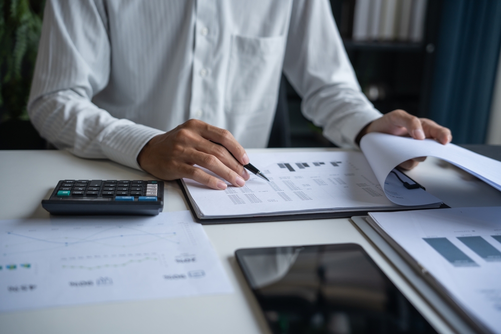 braços de homem de camisa social branca e papeis e anotações sobre mesa de escritório