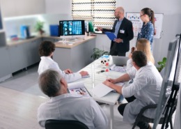 médicos reunidos em sala de reunião com gestor apresentando algo em tela