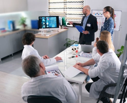 médicos reunidos em sala de reunião com gestor apresentando algo em tela