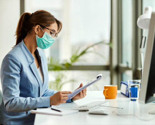 gestora de saúde em mesa de trabalho e utilizando máscara facial de proteção de virús