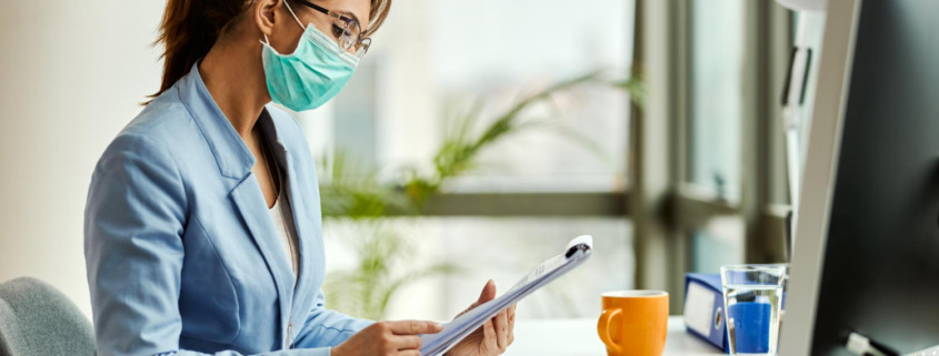 gestora de saúde em mesa de trabalho e utilizando máscara facial de proteção de virús