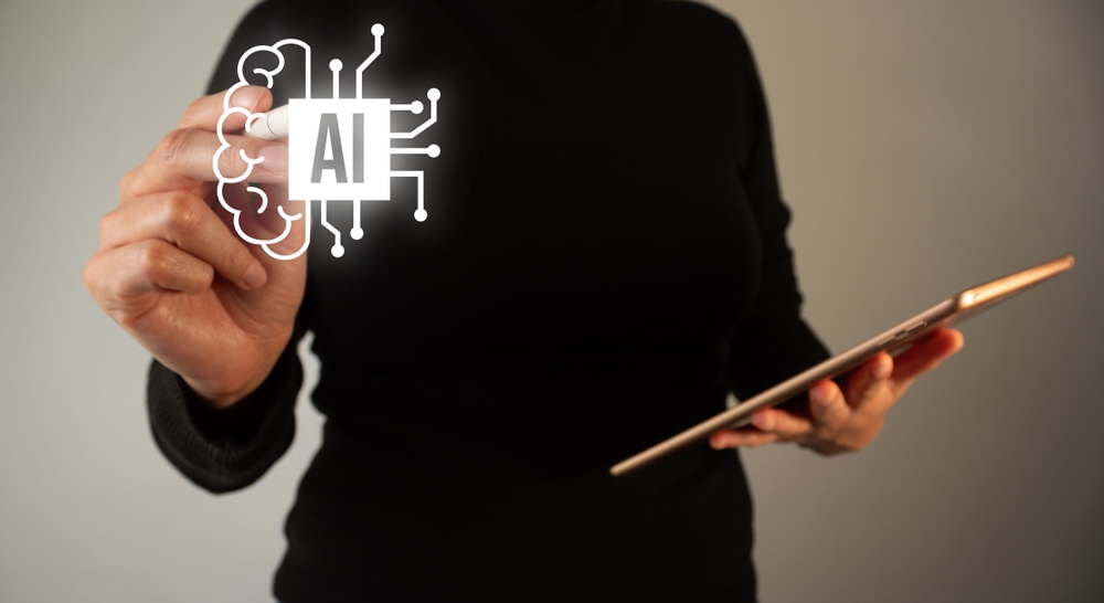 pessoa em pé com um tablet em uma mão e apontando o dedo para um quadro virtual escrito AI