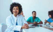 médica em mesa de reunião com outros médicos ao lado