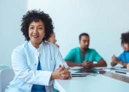 médica em mesa de reunião com outros médicos ao lado