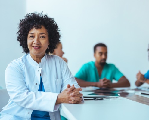 médica em mesa de reunião com outros médicos ao lado