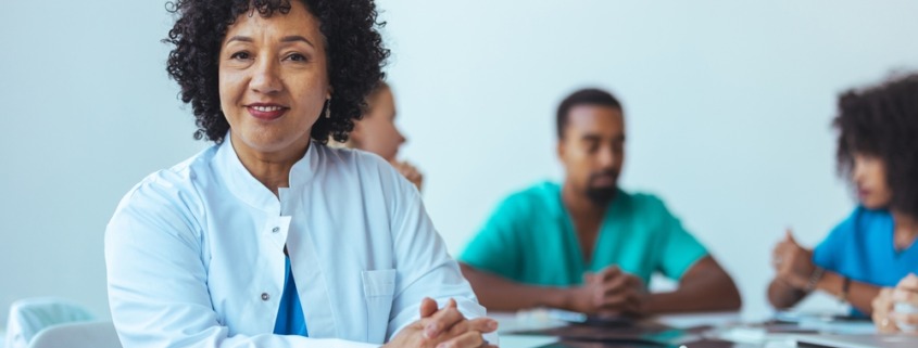 médica em mesa de reunião com outros médicos ao lado