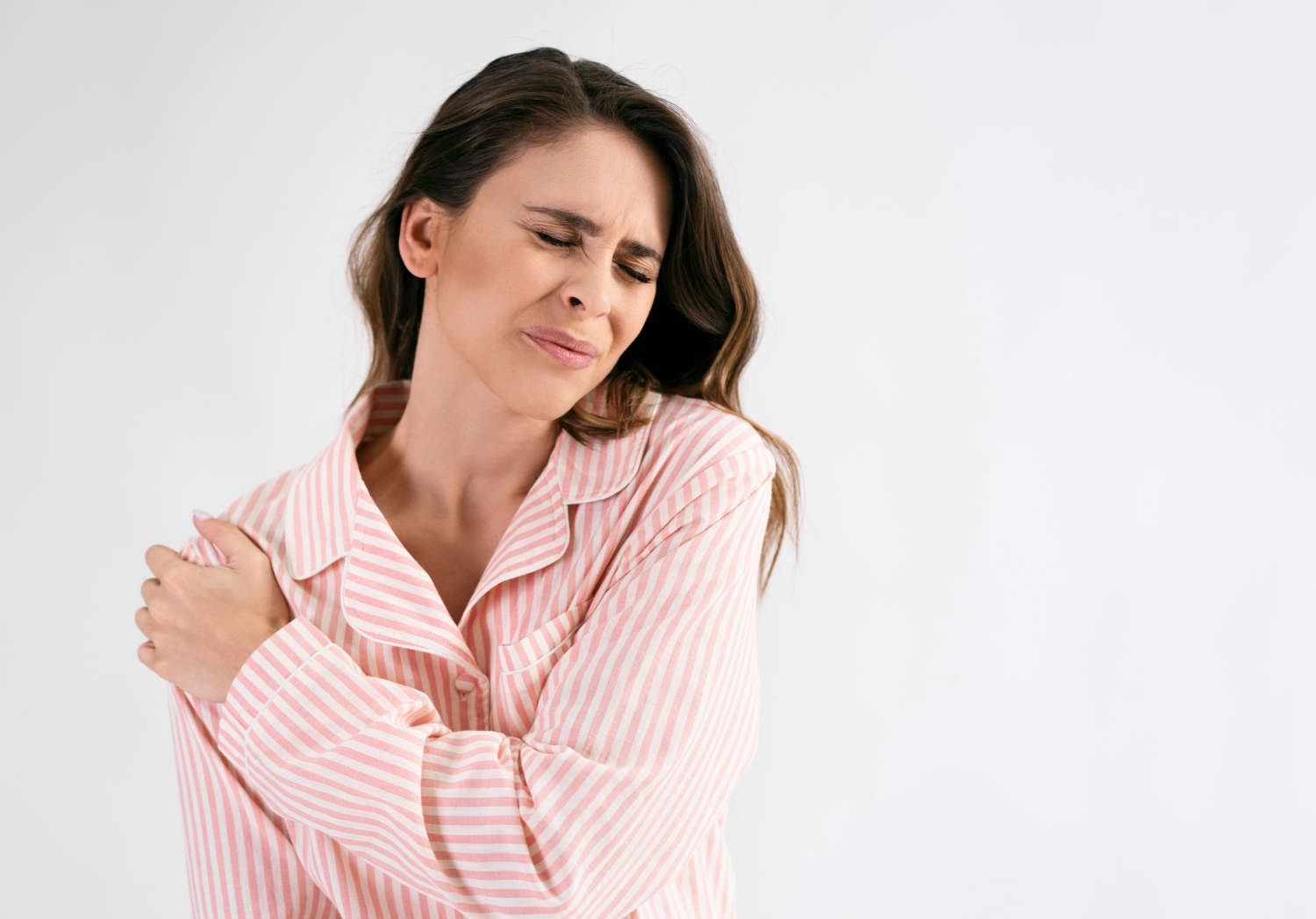 mulher em pé com expressão de dor e com a mão no ombro