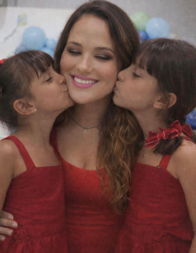 mãe sorrindo ao centro sendo beijada pelas duas filhas