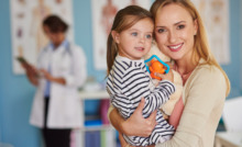 mãe segurando a filha no colo com médica ao fundo