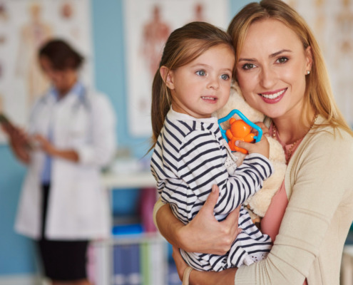 mãe segurando a filha no colo com médica ao fundo