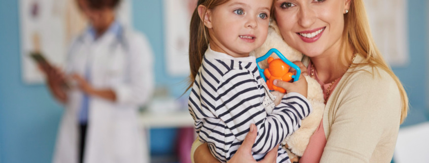 mãe segurando a filha no colo com médica ao fundo