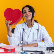 médica em mesa de trabalho seguranddo um coração de pelúcia