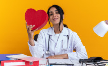 médica em mesa de trabalho seguranddo um coração de pelúcia