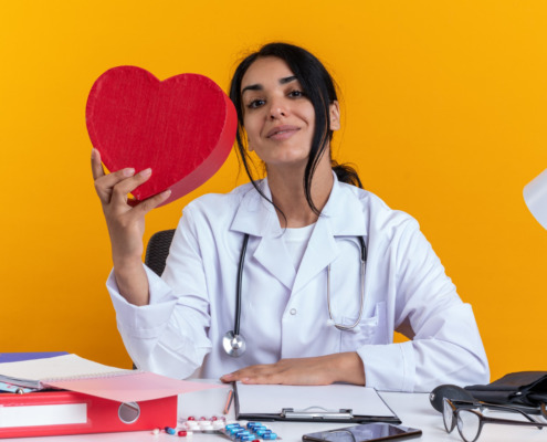 médica em mesa de trabalho seguranddo um coração de pelúcia