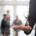 pessoa em pé em sala de reunião com ampulheta na mão e ao fundo outras pessoas de terno