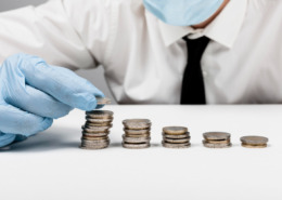 Pessoa com máscara e proteção e luva descartável colocando moedas na mesa indicando economia