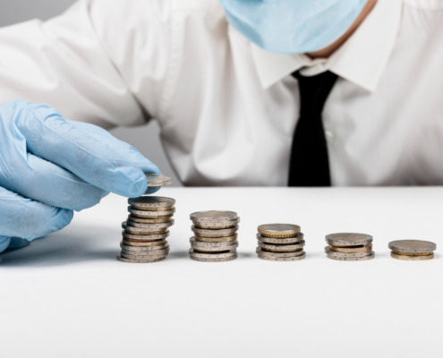 Pessoa com máscara e proteção e luva descartável colocando moedas na mesa indicando economia