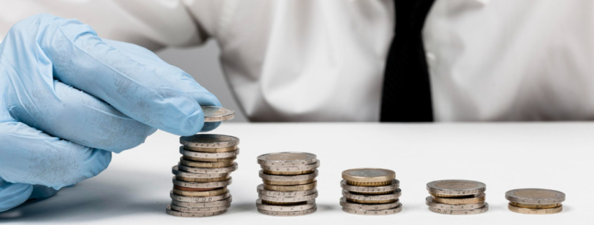 Pessoa com máscara e proteção e luva descartável colocando moedas na mesa indicando economia