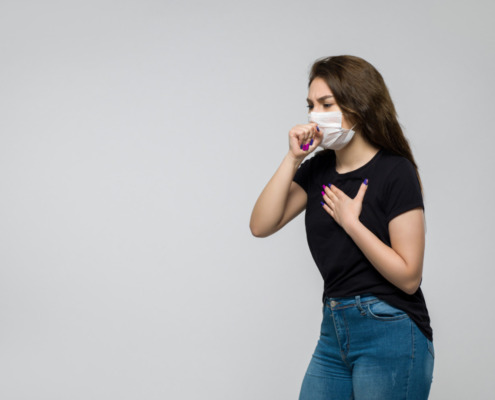 pessoa com máscara de proteção no rosto tossindo, indicando problemas respiratórios