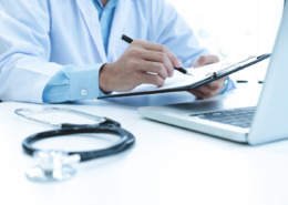 médico em consultório utilizando notebook e preenchendo documentos