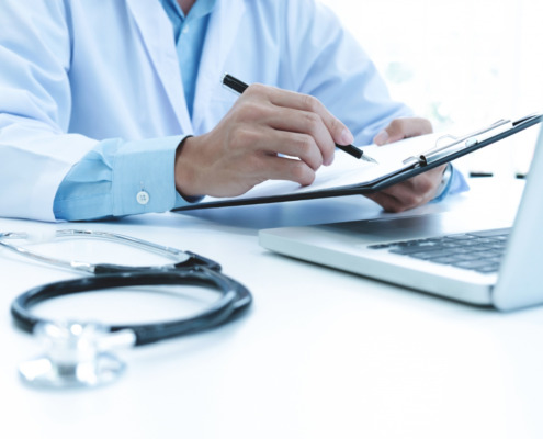 médico em consultório utilizando notebook e preenchendo documentos