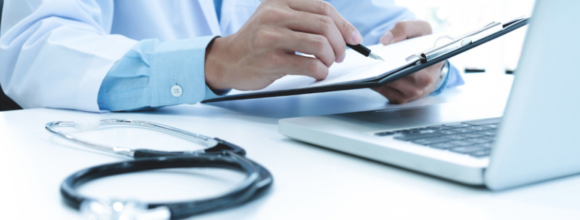 médico em consultório utilizando notebook e preenchendo documentos